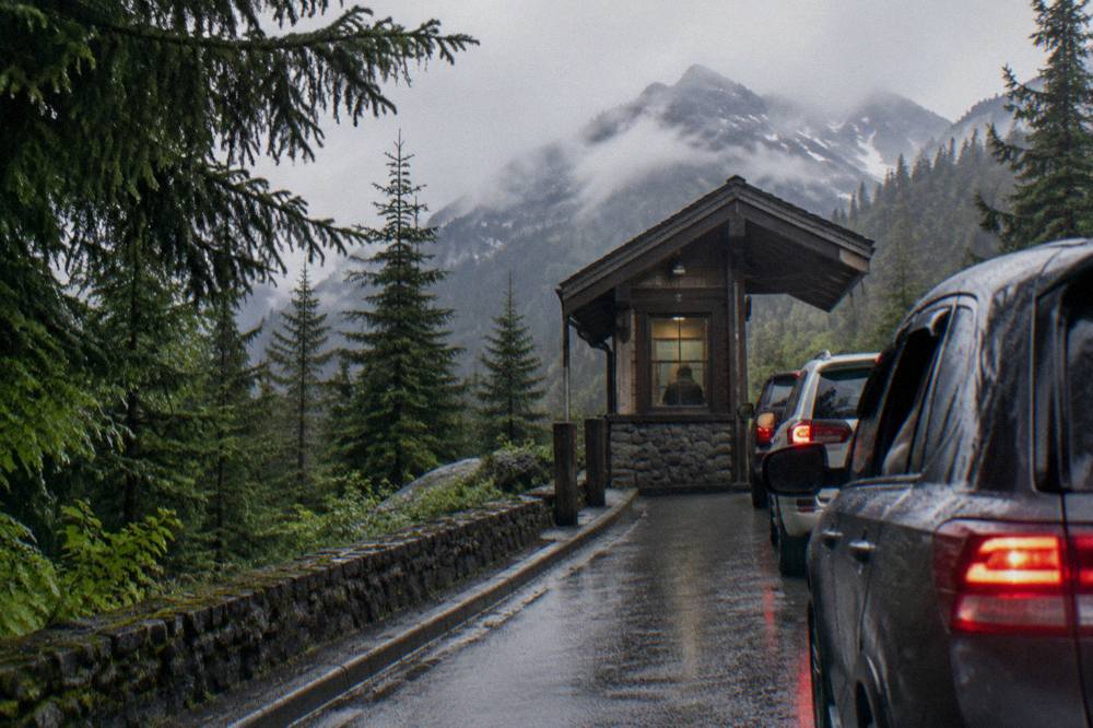 An entrance station booth on a forested park road with a line of cars waiting