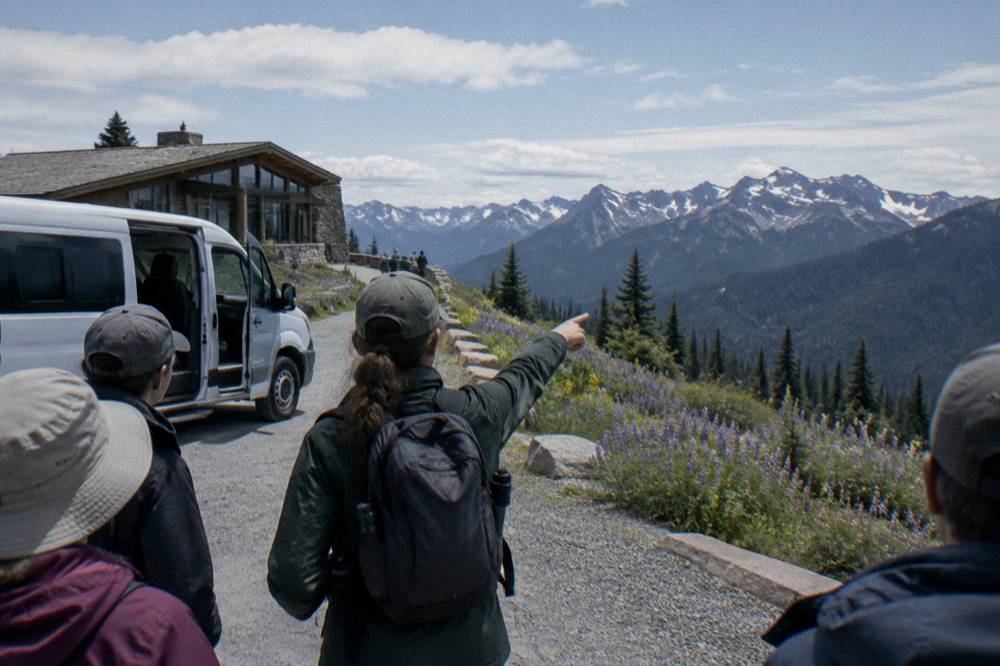 Small tour van parked at a forest overlook with a guide pointing toward the ridge